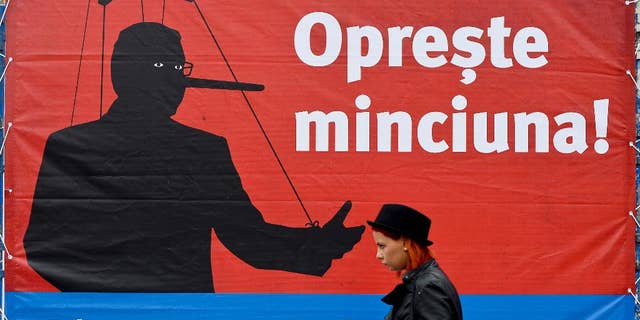 A woman walks backdropped by a campaign poster of Klaus Iohannis leader of Romania's centre-right Liberals and mayor of the Transylvanian city of Sibiu, showing a mock representation of Prime Minister and candidate of the ruling Social Democracy Party (PSD) together with the texts "Stop the lying!" and "Choose the normal Romania!", in Bucharest, Romania, Monday, Nov. 10, 2014. Top party lieutenants in Ponta’s Social Democratic Party, regular party members and other supporters have been convicted or are being probed for corruption, but Ponta appears unscathed. An election runoff will be held on Nov. 16., to elect a new leader as President Traian Basescu steps down after 10 years in office. (AP Photo/Octav Ganea, Mediafax) ROMANIA OUT