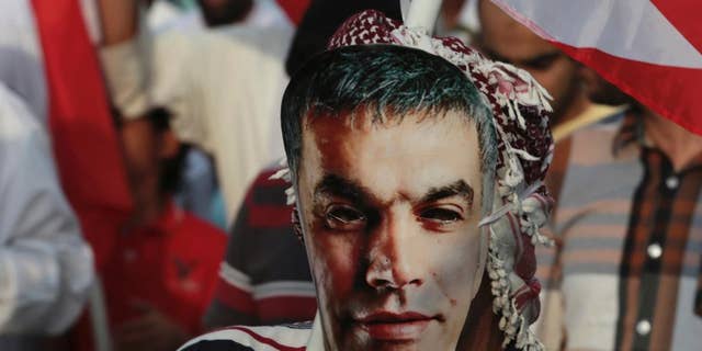 FILE - In this Friday, March 21, 2014 file photo, a Bahraini pro-democracy protester wears a mask with an image of jailed Bahraini human rights activist Nabil Rajab as others wave national flags during a march in Abu Saiba, west of the capital, Manama, Bahrain. The country's official news agency reported Monday, July 13, 2015, that King Hamad bin Isa Al Khalifa has pardoned Rajab, an outspoken human rights activist on health grounds after three months in prison. (AP Photo/Hasan Jamali, File)