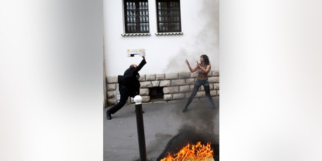 EDS NOTE: NUDITY - A man throws a box toward a FEMEN activist during a protest in front of the Grand Mosque in Paris, Wednesday, April 3, 2013. The radical feminists, calling for more sexual freedom for Arab women, were protesting in support of a young Tunisian woman who received online death threats from ultraconservative Muslims after posting topless photos of herself online. (AP Photo/Christophe Ena)