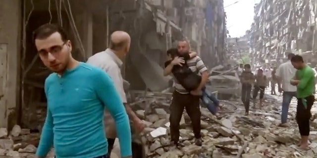April 28, 2016 image made from video and posted online from Validated UGC, a man carries a child after airstrikes hit Aleppo, Syria.