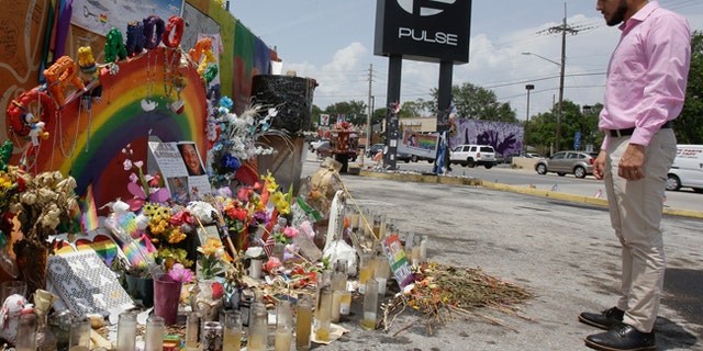 In this Tuesday, May 30, 2017 photo, Marco Quiroga, who works to support LGBTQ and social-justice causes in central Florida, reflects in front of one of the memorials at the Pulse Nightclub in Orlando, Fla. A year after the Pulse Nightclub shooting, the city's gay Latinos are trying to build up their community by forming support groups, seeking seats at the tables of power and creating a foundation to champion gays and Latinos. (AP Photo/John Raoux)