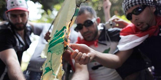 Protesters set fire to a Hezbollah flag, during an anti-Syrian regime rally near the Syrian embassy in Cairo, Egypt. Syrian troops fired Tuesday on residents who set up makeshift roadblocks to prevent the advance of tanks ringing the city of Hama, which has become a flashpoint of the uprising against autocratic President Bashar Assad, activists said.