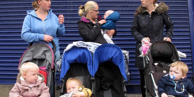 Keira Firth, left, Jessica Clarkson, center, and Jodie Britton stand with their children for the photographer in Birstall, England, Saturday June 18, 2016, after laying floral tributes for Jo Cox, the 41-year-old British Member of Parliament shot and stabbed to death Thursday. Both Britton and her friend, Jessica Clarkson, had come to pay respects to Cox after both received help from the lawmaker in fixing problems with their state-provided homes. (AP Photo/Shawn Pogatchnik)