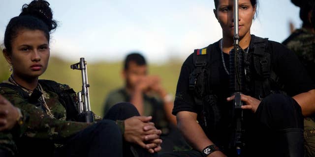 FILE - In this Jan. 4, 2016, file photo, Juliana, 20, left, and Mariana, 24, rebel soldiers for the 36th Front of the Revolutionary Armed Forces of Colombia, or FARC, listen to a commander speak on the peace negotiations between the rebels and the Colombian government, in a hidden camp in Antioquia state, in the northwest Andes of Colombia. Colombian President Juan Manuel Santos said Tuesday, June 21, that his government may reach an agreement on a bilateral ceasefire with leftist rebels as early as this week. (AP Photo/Rodrigo Abd,File)