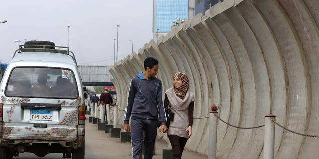 Egyptian couple walks past a concrete barrier surrounding the foreign ministry in Cairo, Egypt, Thursday, Nov. 27, 2014. Egypt's interior minister warned Tuesday that his forces will use deadly force to counter any assault against public facilities in a message coming just ahead of a planned protest by Islamists. (AP Photo/Amr Nabil)