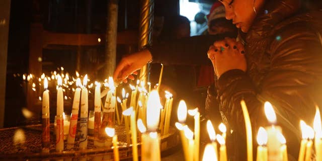 A Christian worshipper prays after lighting a candle on Christmas Eve at the Church of the Nativity, built atop the site where Christians believe Jesus Christ was born, in the West Bank City of Bethlehem, Saturday, Dec. 24, 2016. (AP Photo/Majdi Mohammed)