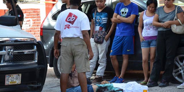 People stand next to the body of police commander David Urquizo Molina after he was gunned down in the city of Chilpancingo, Guerrero State, Mexico, Thursday, July 30, 2015. About two hours later, authorities pursuing the suspected gunmen killed three. Three others were wounded and seven were arrested. Guerrero has been racked with violence as competing drug cartels clash frequently with police and soldiers. (AP Photo/Alejandrino Gonzalez)