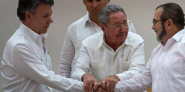 In this Wednesday, Sept. 23, 2015 photo, Cuba's President Raul Castro, center, encourages Colombian President Juan Manuel Santos, left, and Commander the Revolutionary Armed Forces of Colombia or FARC, Timoleon Jimenez to shake hands, in Havana, Cuba. In a joint statement, Santos and the FARC said they have overcome the last significant obstacle to a peace deal by settling on a formula to compensate victims and punish belligerents for human rights abuses. (AP Photo/Desmond Boylan)