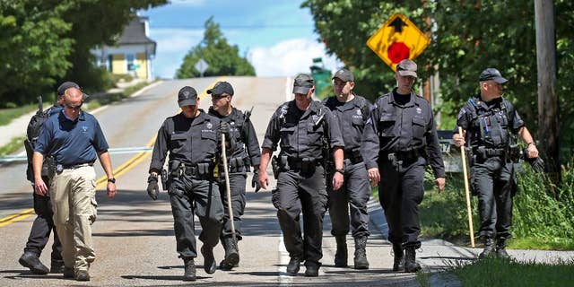 State Police walk down the street after searching through the woods for evidence after a woman visiting her mother was found slain, Aug. 9, 2016 in Princeton, Massachusetts. 