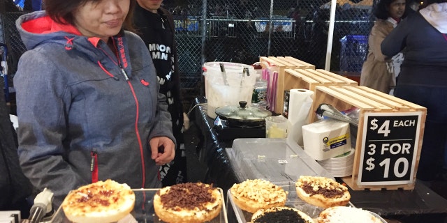 Vendors at the Queens Night Market in New York City's Corona, Queens, neighborhood, selling Indonesian coconut cake snacks with various toppings.