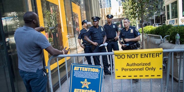 In this Thursday, Aug. 10, 2017 photo, police officers give a pedestrian directions while standing guard outside Trump Tower in New York. Donald Trump plans to come home to Trump Tower for a few days starting Sunday, the first time since his inauguration. New York City police are planning a slight security clampdown in the area around the skyscraper for the duration of his visit. (AP Photo/Mary Altaffer)