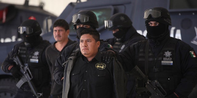 Federal Police agents escort Flavio Mendez Santiago, center, alias "El Amarillo," alleged member and co-founder of the Zetas drug cartel, during a presentation to the media in Mexico City, Tuesday, Jan. 18, 2011. Mendez Santiago was detained in Villa de Etla, Mexican state of Oaxaca, some 400 km southeast of Mexico City, on Monday. (AP Photo/Alexandre Meneghini)