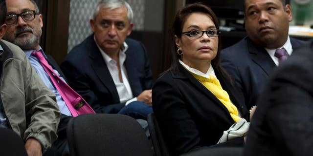 FILE - In this April 20, 2016, file photo, Guatemala's former Vice-President Roxana Baldetti, wearing a yellow scarf, and former President Otto Perez Molina, back center, wait for the start of a court hearing in Guatemala City. Perez and Baldetti have been formally charged on Thursday, June 16, 2016, in a sprawling corruption scheme that emptied government coffers and laundered money to be spent on Miami shopping sprees, real estate and luxury vehicles. (AP Photo/Moises Castillo, File)