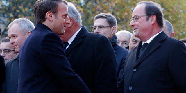 French President Emmanuel Macron, left, shakes hands with former French President Francois Hollande as they stand in front of a commemorative plaque outside the Stade de France stadium, in Saint-Denis, near Paris, Monday, Nov. 13, 2017.