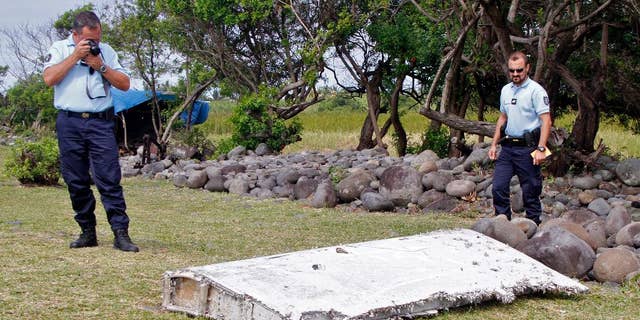 FILE - In this July 29, 2015 file photo, French police officers look over a piece of debris from a plane in Saint-Andre, Reunion Island. The wing was later found to be from missing Malaysia Airlines Flight 370 that went missing March 8, 2014, with 239 people aboard while flying from Kuala Lumpur to Beijing. Analysis of a genuine Boeing 777 wing flap has reaffirmed experts' opinion that a missing Malaysian airliner most likely crashed north of an abandoned search area in the Indian Ocean, officials said Friday, April 21, 2017. The search for Malaysia Airlines Flight 370 ended in January after a deep-sea sonar scan failed to find any trace of the plane. But research has continued in an effort to refine a possible new search. (AP Photo/Lucas Marie, File)