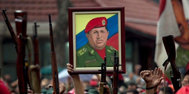 FILE - In this April 13, 2010 file photo, members of the National Revolutionary Militia hold up their weapons and a painting of Venezuela's President Hugo Chavez at an event marking the 9th anniversary of Chavez's return to power after a failed 2002 coup, in Caracas, Venezuela. Venezuela has found yet another way to honor the late leader who launched Venezuelaâs socialist revolution. A state-sponsored ballet about his life premieres on Saturday, Nov. 29, 2014, with dozens of performers recounting Chavezâs life, from humble roots, to failed coup, to international fame. (AP Photo/Ariana Cubillos, File)