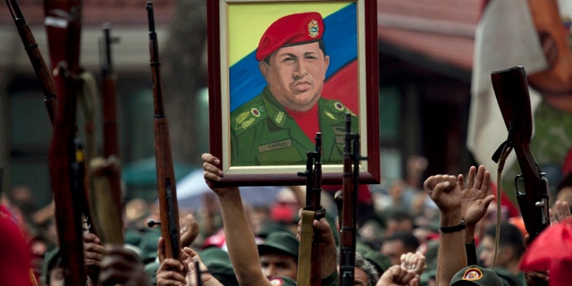 FILE - In this April 13, 2010 file photo, members of the National Revolutionary Militia hold up their weapons and a painting of Venezuela's President Hugo Chavez at an event marking the 9th anniversary of Chavez's return to power after a failed 2002 coup, in Caracas, Venezuela. Venezuela has found yet another way to honor the late leader who launched Venezuelaâs socialist revolution. A state-sponsored ballet about his life premieres on Saturday, Nov. 29, 2014, with dozens of performers recounting Chavezâs life, from humble roots, to failed coup, to international fame. (AP Photo/Ariana Cubillos, File)