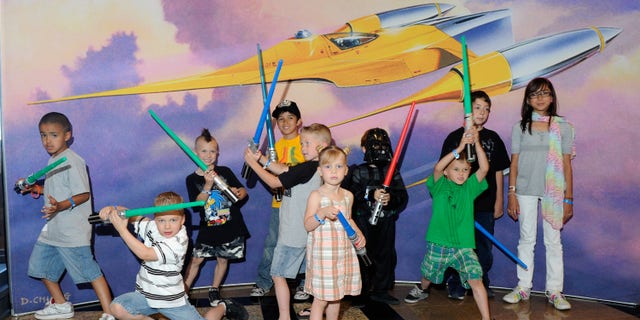 LAS VEGAS - MAY 29: Kids with toy lightsabers pose in front of Star Wars artwork at the museum exhibit of "Star Wars: In Concert" at the Orleans Arena May 29, 2010 in Las Vegas, Nevada. The traveling production features a full symphony orchestra and choir playing music from all six of John Williams' Star Wars scores synchronized with footage from the films displayed on a three-story-tall, HD LED screen. (Photo by Ethan Miller/Getty Images)