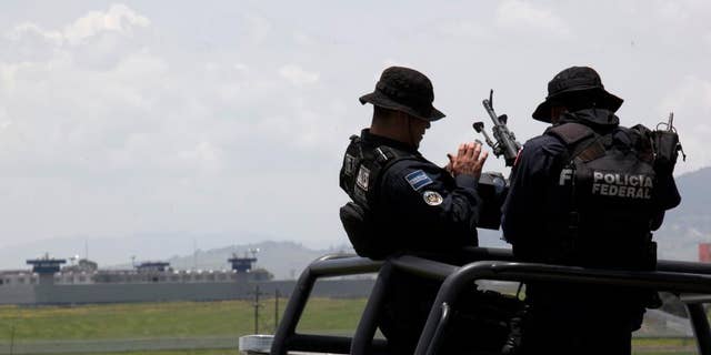 Federal Police man their weapons aboard a pick up truck, near the half-built house where drug lord Joaquin "El Chapo" Guzman made his escape through a tunnel from the Altiplano maximum security prison in Almoloya, west of Mexico City, Monday, July 13, 2015. The Altiplano prison can be seen in the background. A widespread manhunt that included highway checkpoints, stepped up border security and closure of an international airport failed to turn up any trace of "El Chapo" Guzman by Monday, more than 24 hours after he escaped through an underground tunnel in his cell. (AP Photo/Marco Ugarte)