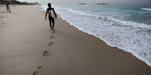 A surfer walks next to the shore at Barra da Tijuca beach before the start of the Billabong Rio Pro surfing championship in Rio de Janeiro, Brazil, Thursday, May 12, 2011. (AP Photo/Victor R. Caivano)