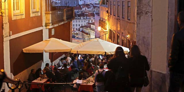 FILE - In this May 25, 2016 file photo, tourists have dinner at restaurant tables set outside with a view of Saint George castle in the background, in Lisbon. Portugal's fragile economy is getting a tonic from tourism this year, with revenue up by more than 10 percent through October including a 20 percent jump in visitors from the United States. Tourism minister Ana Mendes Godinho says the sector brought in some 11 billion euros ($11.5 billion) in the first 10 months of 2016 — about 1 billion euros more than the same period last year. (AP Photo/Armando Franca)
