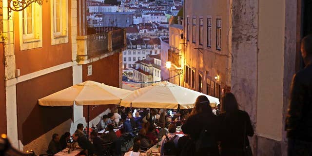 FILE - In this May 25, 2016 file photo, tourists have dinner at restaurant tables set outside with a view of Saint George castle in the background, in Lisbon. Portugal's fragile economy is getting a tonic from tourism this year, with revenue up by more than 10 percent through October including a 20 percent jump in visitors from the United States. Tourism minister Ana Mendes Godinho says the sector brought in some 11 billion euros ($11.5 billion) in the first 10 months of 2016 — about 1 billion euros more than the same period last year. (AP Photo/Armando Franca)