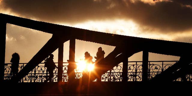 People walk over a pedestrian bridge over the river Main as the sun sets in Frankfurt, central Germany, Monday, Jan. 16, 2017. (AP Photo/Michael Probst)