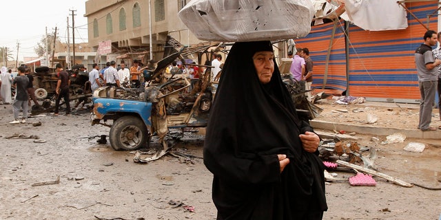 An Iraqi woman, who sells milk, passes by the scene of a car bomb attack in the Kamaliyah neighborhood, a predominantly Shiite area of eastern Baghdad, Iraq, Monday, May 20, 2013. A wave of car bombings across Baghdad's Shiite neighborhoods and in the southern city of Basra killed and wounded scores of people, police said. (AP Photo/ Hadi Mizban)