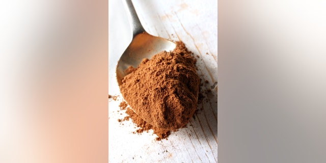 Cocoa powder on an old silver spoon, on rough wooden surface.