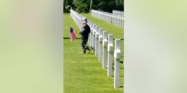 A young visitor carrying the U.S. flag walks among graves at the Colleville American military cemetery, in Colleville sur Mer, western France, Saturday June 6, 2015,  on  the 71th anniversary of the D-Day landing.  D-Day marked the start of a Europe invasion, as many thousands of Allied troops began landing on the beaches of Normandy in northern France in 1944 at the start of a major offensive against the Nazi German forces, an offensive which cost the lives of many thousands. (AP Photo/Remy de la Mauviniere)