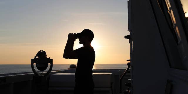 A U.S. Coast Guard crew member scans the horizon with his binoculars just outside the bridge of the USCG Cutter Stratton in the eastern Pacific Ocean, Feb. 22, 2017. (Associated Press)