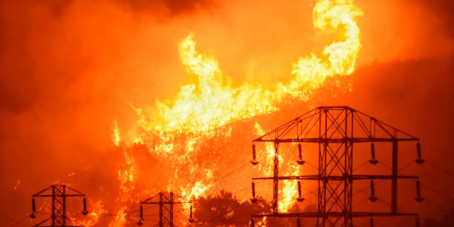 In this Saturday, Dec. 16, 2017, photo provided by the Santa Barbara County Fire Department, flames burn near power lines in Sycamore Canyon near West Mountain Drive in Montecito, Calif.