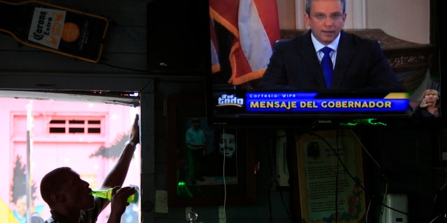 A man drinks a beer in a local bar as he watches Puerto Ricoâs governor Alejandro Garcia Padilla on television delivering an address on the state of the island's finances, in San Juan, Puerto Rico, Monday, June 29, 2015. The governor said that he will form a financial team to negotiate with bondholders on delaying debt payments and then restructuring $72 billion in public debt that he says the island can't repay. (AP Photo/Ricardo Arduengo)