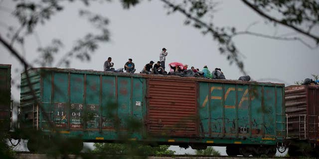 FILE - In this June 20, 2014 file photo, Central American migrants wait atop the freight train they had been traveling north on, as it starts to rain after the train suffered a minor derailment outside Reforma de Pineda, Chiapas state, Mexico. Mexico now deports more Central American migrants than the United States, a dramatic shift since the U.S. asked Mexico for help a year ago with a spike in illegal migration, especially among unaccompanied minors. (AP Photo/Rebecca Blackwell, File)