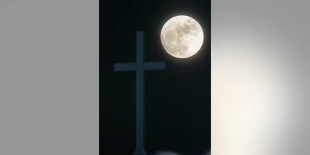 The Long Night Moon rises behind a cross at Christ Community Church in Lawrence, Kan., Thursday, Dec. 24, 2015. When the moon turns full, at 5:11am cst., it will be the first full moon to fall on Christmas day since 1977. Named the Long Night Moon because it's the first full moon to follow the winter solstice, it's also known as the Cold Moon. (AP Photo/Orlin Wagner)