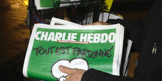 FILE - In this Wednesday, Jan. 14, 2015, file photo, a seller of newspapers stocks several Charlie Hebdo newspapers at a newsstand in Nice, France. The French satirical newspaper Charlie Hebdo will publish a German version in the country that has given the best reception to the weekly paper outside France since the attacks that wiped out the Paris editorial staff in January 2015. (AP Photo/ Lionel Cironneau, File)