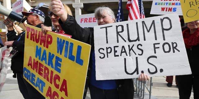 FILE - In this Feb. 4, 2017, file photo, a woman gives a thumbs up in Los Angeles, Calif., as demonstrators in favor of President Donald Trump's executive order banning travel to the U.S. from seven primarily Muslim nations stand across the street from the Tom Bradley International Terminal at Los Angeles International Airport. President Donald Trump's administration said in court documents on Thursday, Feb. 16, 2017, it wants an end to the legal fight over its ban on travelers from seven predominantly Muslim nations and will instead issue a replacement ban. (AP Photo/Reed Saxon, File)