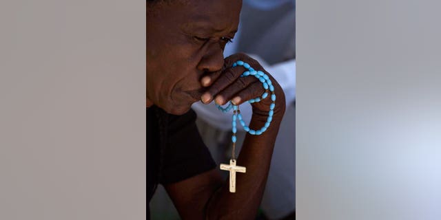 A woman holds a rosary as she prays during a Catholic mass.