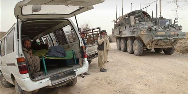 March 11, 2012: An armored military vehicle from the NATO-led International Security Assistance Force (ISAF) is seen at right, as the covered body of a person who was allegedly killed by a U.S. service member is seen.