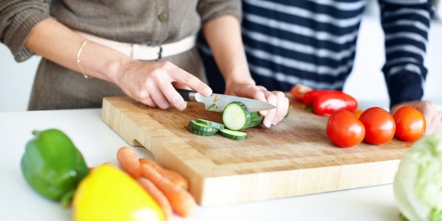 Cropped image of a couple preparing a salad, slicing cucumber on a wooden chopping board