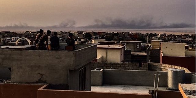 Black smoke from burning tires rises in the distance as Peshmerga fighters keep watch from a post outside Mosul.