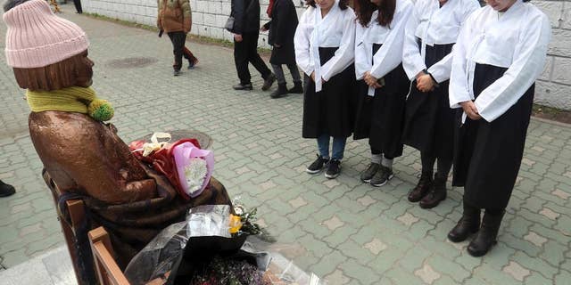 South Korean women wearing traditional dress pay theirs respects to a "comfort-woman" statue set up in front of the Japanese consulate in Busan, South Korea, Friday, Jan. 6, 2017. Japan announced Friday that it would recall its ambassador to South Korea and suspend economic talks in response to the placing of a "comfort-woman" statue representing wartime sex slaves in front of its consulate in the Korean port city of Busan. (Kim Sun-ho/Yonhap via AP)