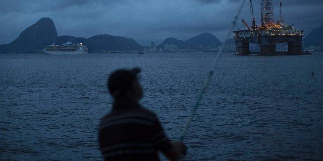 FILE - In this April 21, 2015 file photo, a man fishes in Guanabara Bay where an oil platform floats, backdropped by Sugar Loaf Mountain, left, in Niteroi, Brazil. The Brazilian government on Monday, Sept. 12, 2016 ratified its participation in the Paris Agreement on climate change, a significant step by Latin America’s largest emitter of greenhouse gases that could spur other countries to move forward. (AP Photo/Leo Correa, File)