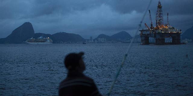 FILE - In this April 21, 2015 file photo, a man fishes in Guanabara Bay where an oil platform floats, backdropped by Sugar Loaf Mountain, left, in Niteroi, Brazil. The Brazilian government on Monday, Sept. 12, 2016 ratified its participation in the Paris Agreement on climate change, a significant step by Latin America’s largest emitter of greenhouse gases that could spur other countries to move forward. (AP Photo/Leo Correa, File)