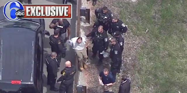 In this frame grab taken from video, Arthur Buckel, center, sits on a guardrail surrounded by police officers after being taken into custody near Double Trouble State Park, Monday, May 9, 2016, in Lacey Township, N.J. The minimum security prison inmate who escaped last week once served time for manslaughter for killing a baby and had been behind bars on assault, drug possession and burglary charges. (AP Photo/ WPVI-TV)