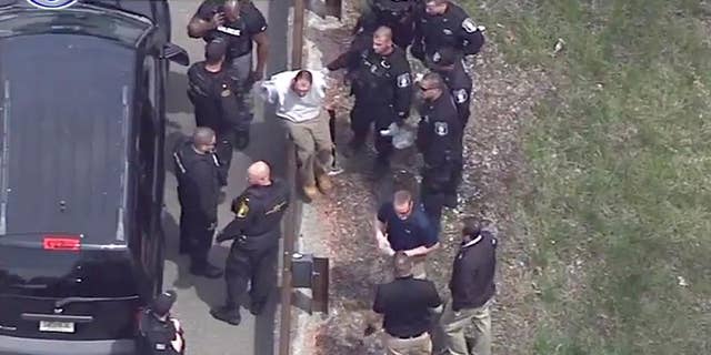 In this frame grab taken from video, Arthur Buckel, center, sits on a guardrail surrounded by police officers after being taken into custody near Double Trouble State Park, Monday, May 9, 2016, in Lacey Township, N.J. The minimum security prison inmate who escaped last week once served time for manslaughter for killing a baby and had been behind bars on assault, drug possession and burglary charges. (AP Photo/ WPVI-TV)