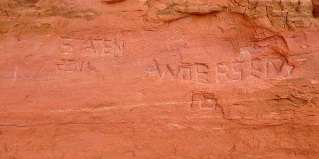 In this April 15, 2016, photo, released by the National Park Service shows carved graffiti at Frame Arch at Arches National Park. Officials at Utah's Arches National Park are investigating large graffiti so deeply carved into one of the park's famous red rock arches that it might be impossible to erase. (Alice deAnguera/National Park Service via AP)