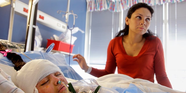 In this Wednesday, March 11, 2015 photo Paola Porter Avila stands over her daughter Paola Matute Porter, 9, in the acute care burn unit of the Shriners Hospitals for Children in Boston. While doctors say Paola Matute's skin grafts are taking well and she is gradually being weaned off pain medication, she will spend a couple more weeks in the hospital before being transferred to a temporary Boston residence to undergo physical therapy. (AP Photo/Stephan Savoia)