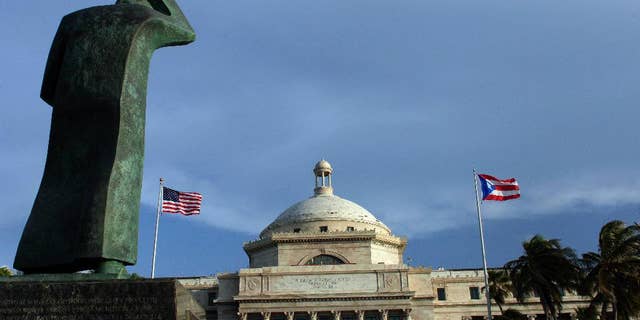 FILE - In this July 29, 2015 file photo, a bronze statue of San Juan Bautista stands in front of Puerto Rico’s capitol flanked by U.S. and Puerto Rican flags, in San Juan. A federal control board on Friday, Sept. 30, 2016, took over Puerto Rico's finances and several government agencies for the first time in the U.S. territory's history in a bid to haul the island out of an acute economic crisis. (AP Photo/Ricardo Arduengo, File)