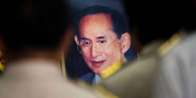 FILE - In this Oct. 6, 2014 file photo, Thai officers offer their respect to a portrait of King Bhumibol Adulyadej at Siriraj Hospital in Bangkok where the 86-year-old king is being treated after he underwent surgery to have his gallbladder removed. A military court in junta-ruled Thailand sentenced a Web editor to 4 1/2 years in jail Monday, Nov. 24 for publishing an article five years ago that it said defamed the nation's king. (AP Photo/Sakchai Lalit, File)